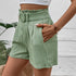 Close-up of sage green textured shorts showing belted paper-bag waist detail and side pocket structure