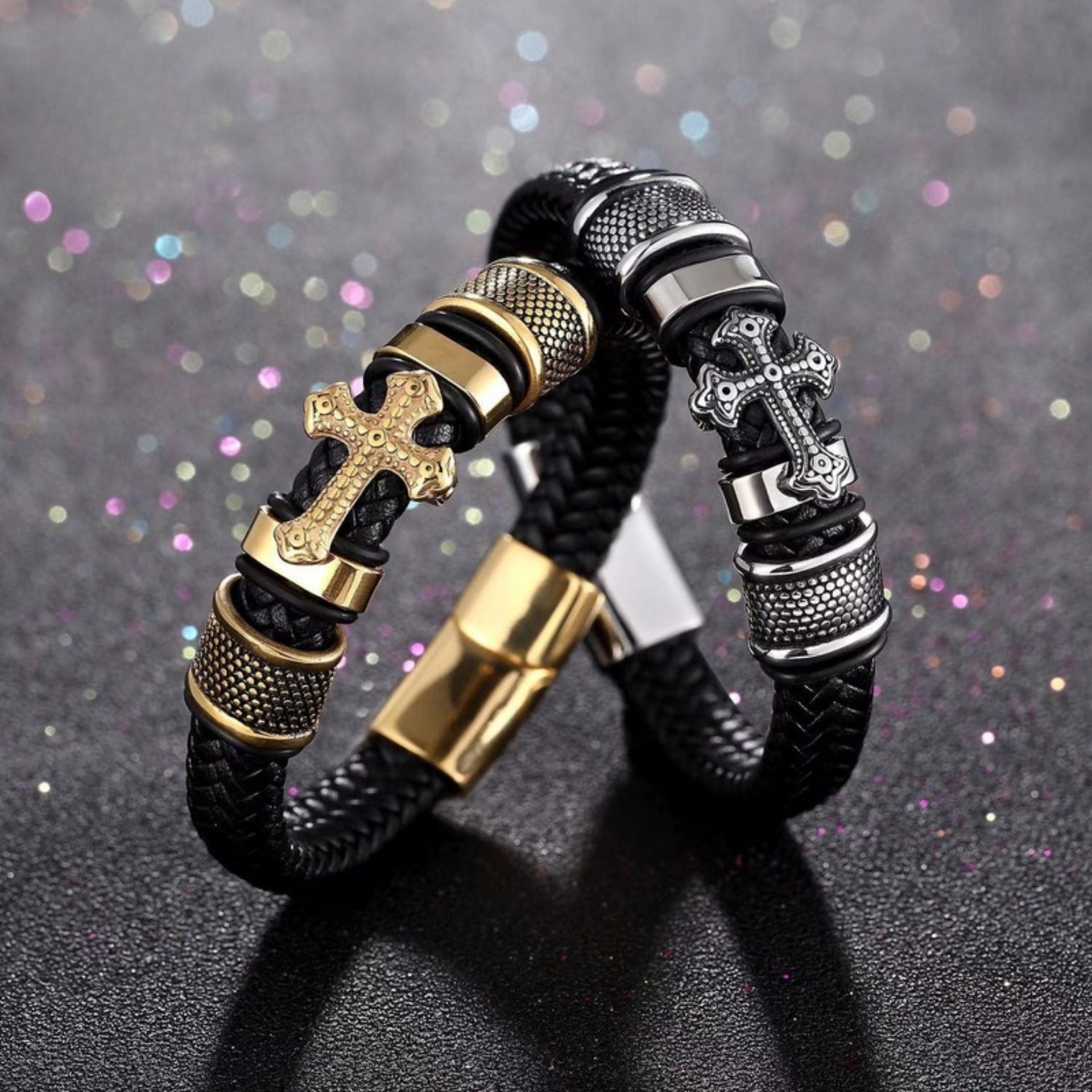 Black braided leather bracelet with gold-tone cross and metallic accents on a glittery background.
