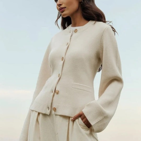 Beige knit cardigan with button detail, model standing in soft light with subtle hand positioning