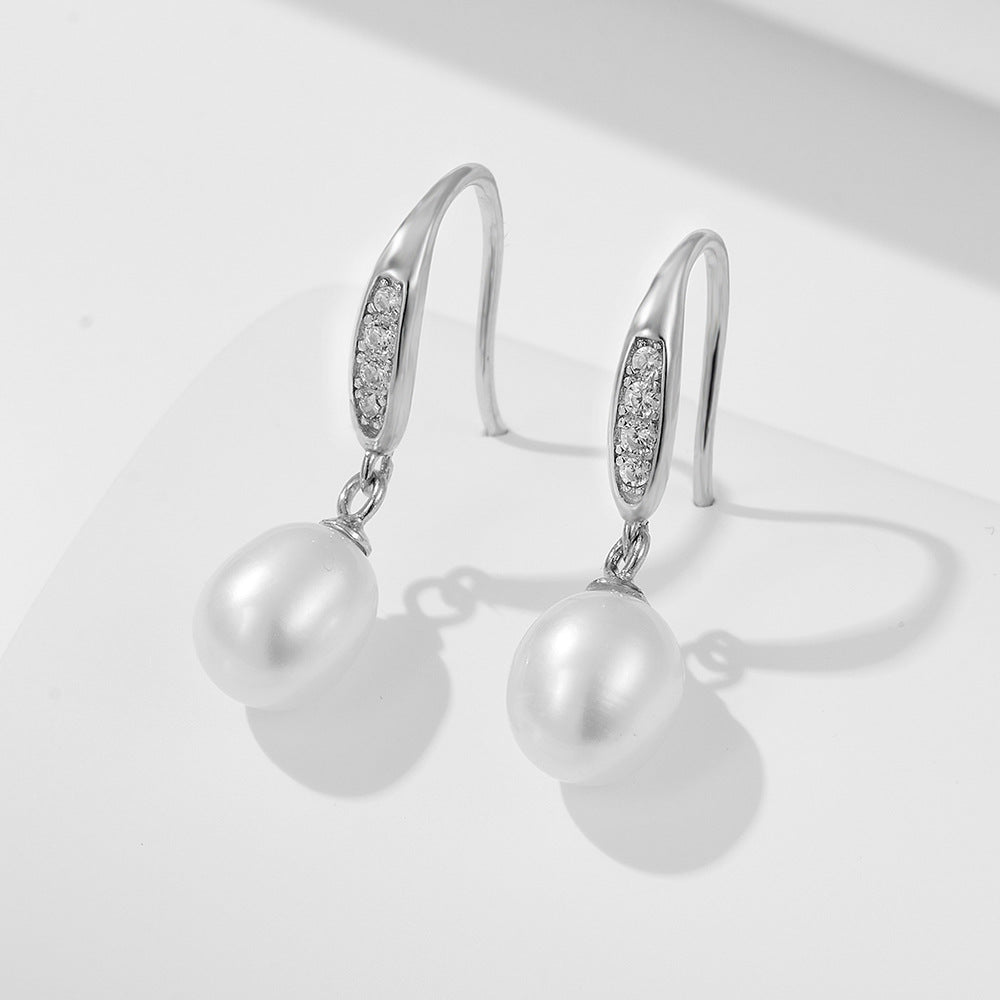 Silver drop earrings with cubic zirconia accents and white pearl pendants on white surface