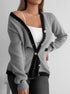 Gray knit cardigan open, showing black trim, gold buttons, and white tank top underneath, in front of white wall