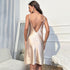 Back view of pearl satin slip dress showing deep V-back design, photographed against white interior setting
