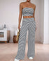 A woman wearing a black and white striped bandeau top and matching wide-leg pants, holding a woven bag, standing in a modern living room.