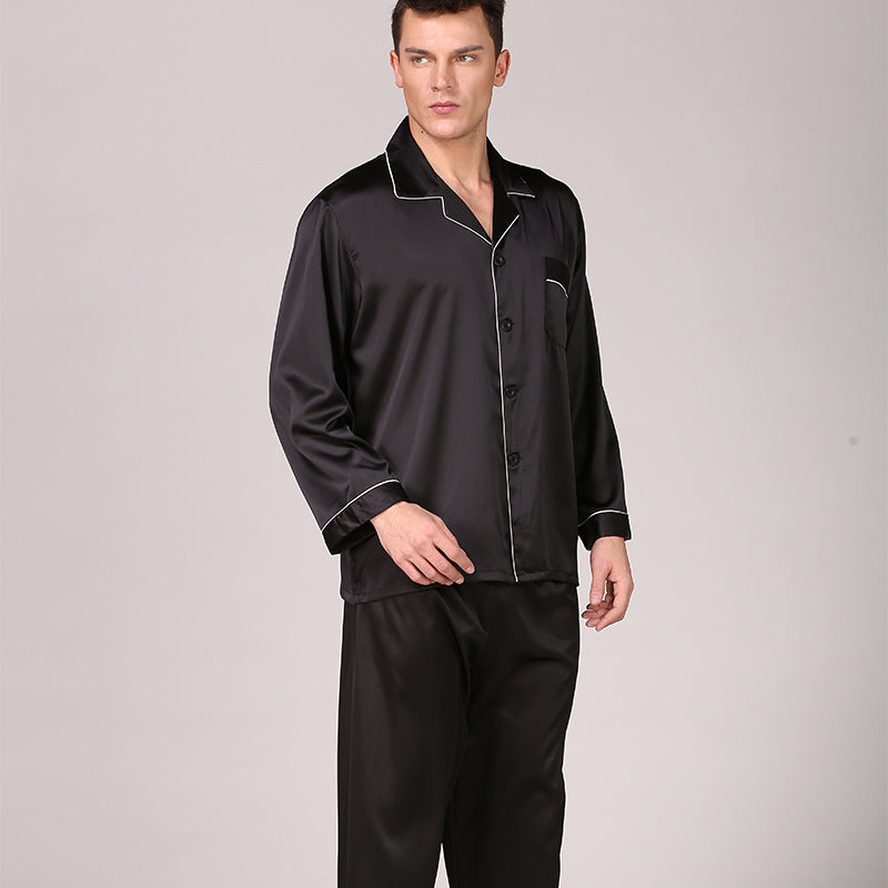 Model wearing black silk pajama set with white piping detail and chest pocket against gray background