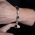  Close-up of a man's wrist wearing a black and gold stainless steel bracelet with a mechanical-inspired link design against a dark background.
