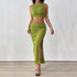 A woman wearing a green two-piece set featuring a ribbed crop top and a matching high-waisted skirt with a ruched side tie and a thigh-high slit, paired with clear high heels.