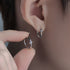 Silver star hoop earring worn on ear, with fingers holding another earring