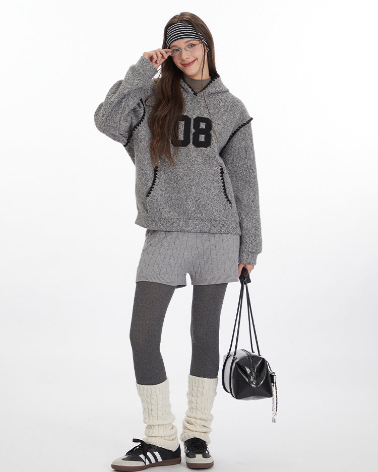 Winter layered look featuring grey textured hoodie with '08' graphic, cable knit shorts over leggings, cream leg warmers, and black sneakers. Styled with black shoulder bag