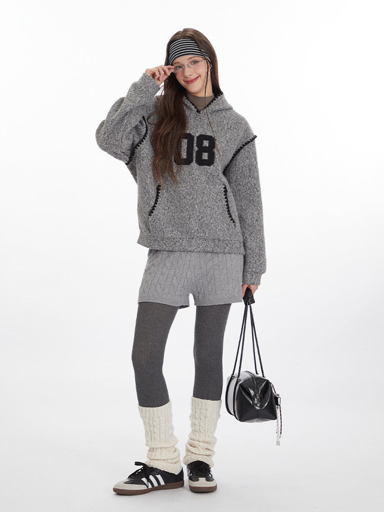Winter layered look featuring grey textured hoodie with '08' graphic, cable knit shorts over leggings, cream leg warmers, and black sneakers. Styled with black shoulder bag