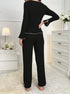 Back view of black ribbed pajama set with white piping, showing straight-leg pants and fitted long-sleeve top against white furniture