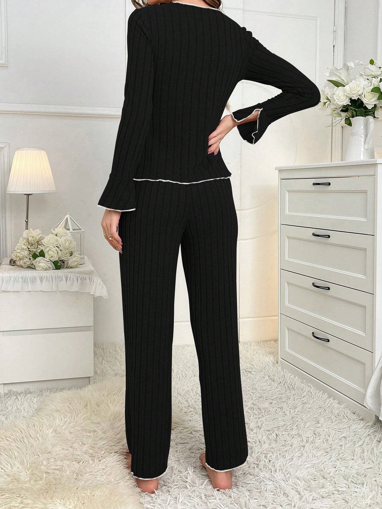 Back view of black ribbed pajama set with white piping, showing straight-leg pants and fitted long-sleeve top against white furniture