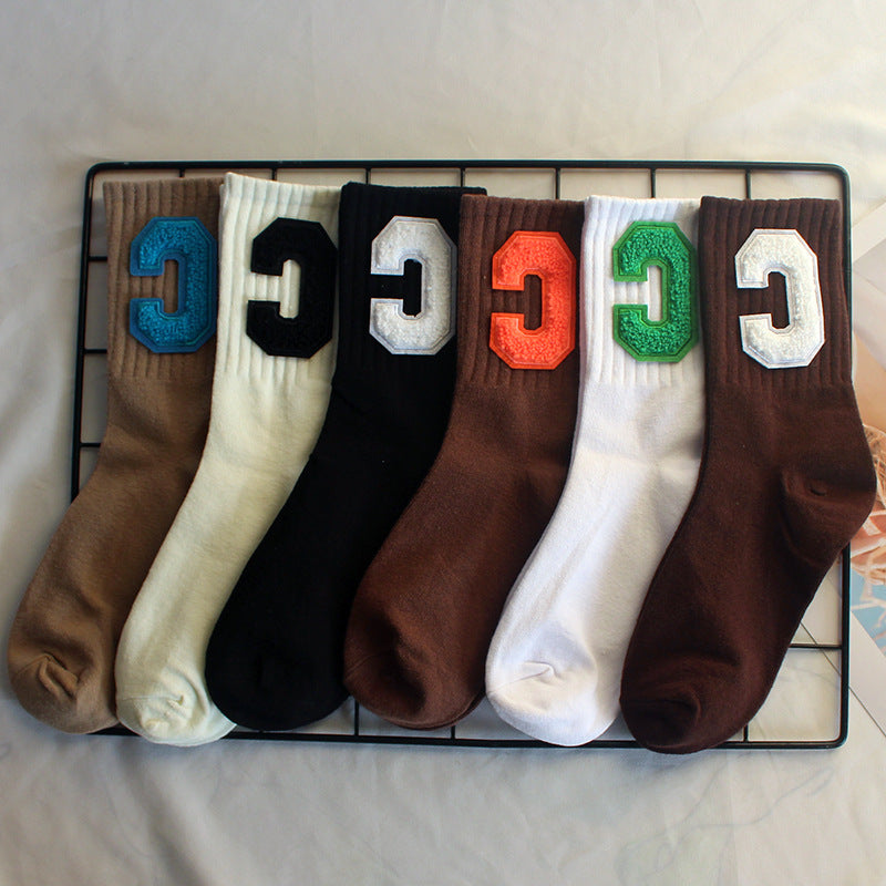 Six pairs of varsity-style crew socks in black, cream, brown, beige, and white, each with a large "C" patch in contrasting colors