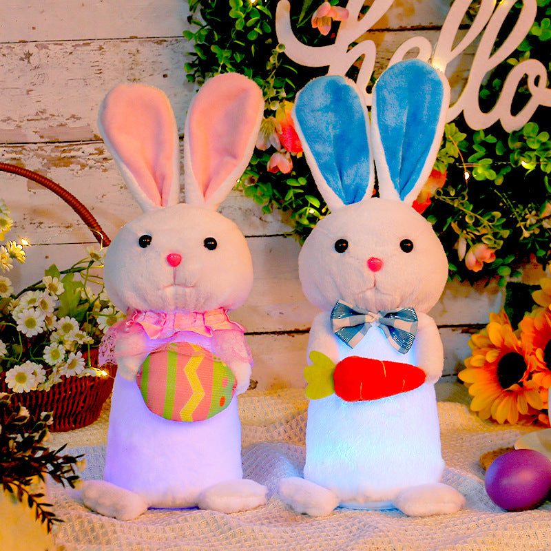 Two plush Easter bunny toys with LED lights, one holding a colorful egg and the other a carrot, set against a rustic floral background with "Hello" signage.