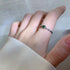 A woman wearing silver chain ring with emerald green stone on finger, hand against white fabric with soft natural lighting