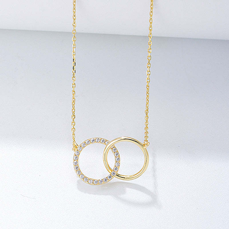 Gold interlocking circles necklace with one pavé diamond circle and one plain circle pendant on delicate chain against white background