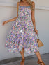 A woman wearing a floral midi dress with spaghetti straps, a drawstring waist, and tiered ruffles. She carries a woven handbag and wears strappy sandals.