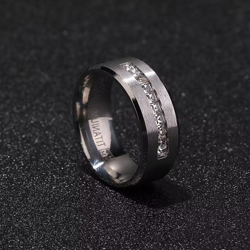 A silver stainless steel ring with embedded square-cut stones, placed on a dark, textured surface for a sleek and modern look.