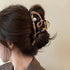 A brown tortoiseshell hair claw clip featuring a heart-shaped open design, a pearl accent, and gold detailing, securing an elegant updo.