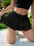 Close-up of black layered ruffle skirt with high waistband, shown on model kneeling on white lace backdrop in garden