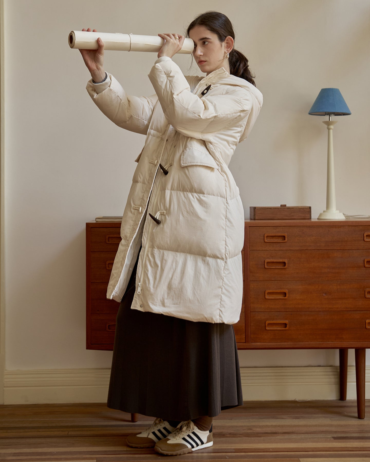 Model holding paper scroll while wearing white down duffle coat, pairing with long skirt and retro sneakers
