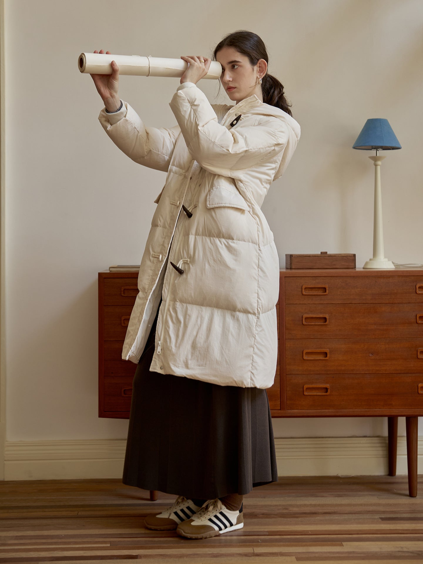 Model holding paper scroll while wearing white down duffle coat, pairing with long skirt and retro sneakers