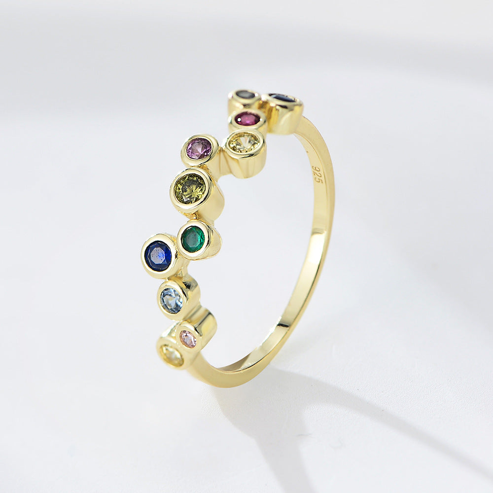 A woman wearing gold bubble rainbow ring with colorful gemstones in bezel settings on white background