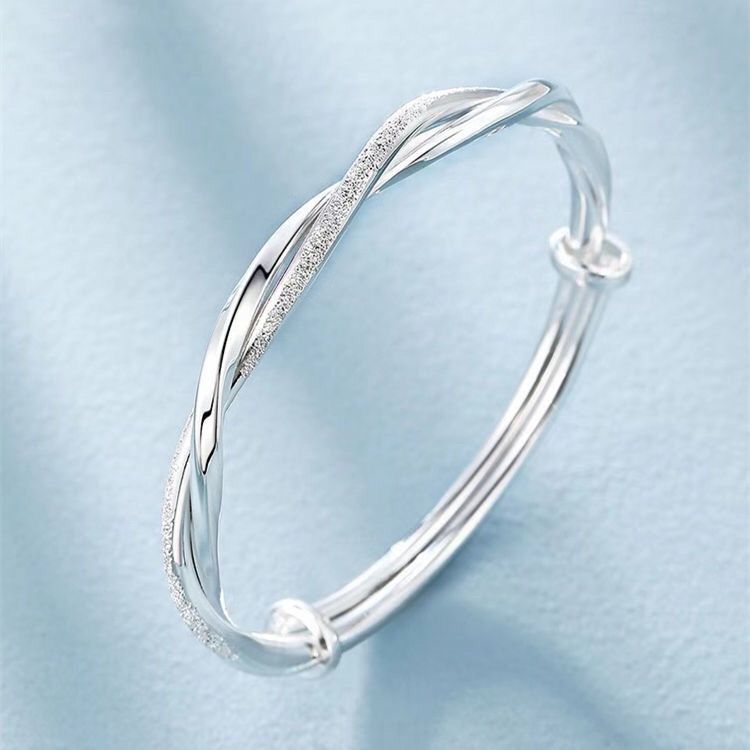 A silver twisted bangle bracelet with one strand adorned with crystals, displayed on pale blue background