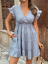 Woman in a baby blue ruffle sleeve babydoll dress with a V-neckline and tiered skirt, standing in front of a wooden door.