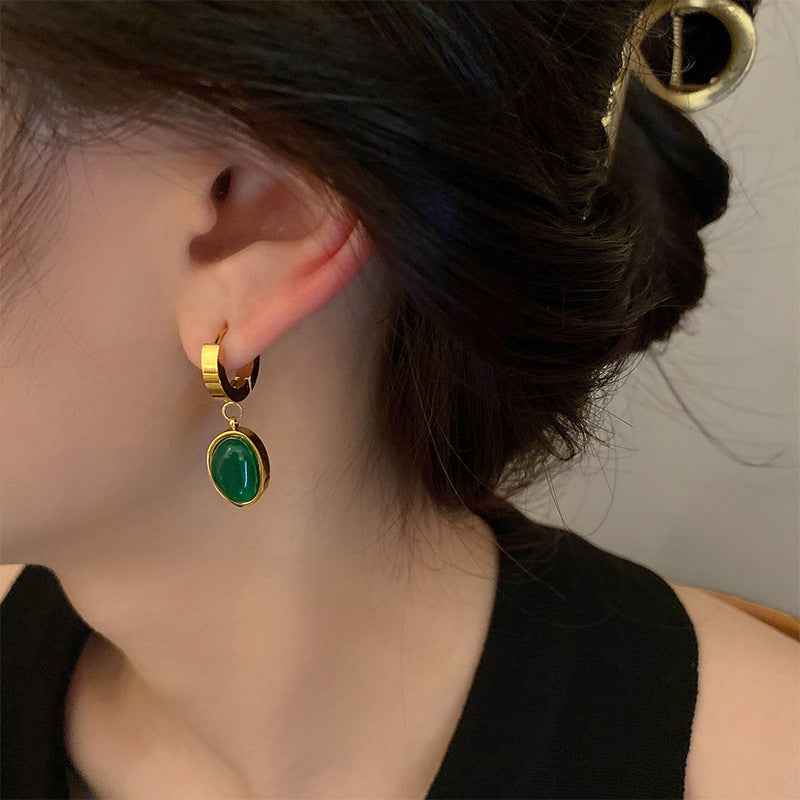 Close-up of woman wearing gold hoop earrings with emerald green oval pendant on white background showcasing elegant jewelry design
