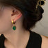 Close-up of woman wearing gold hoop earrings with emerald green oval pendant on white background showcasing elegant jewelry design