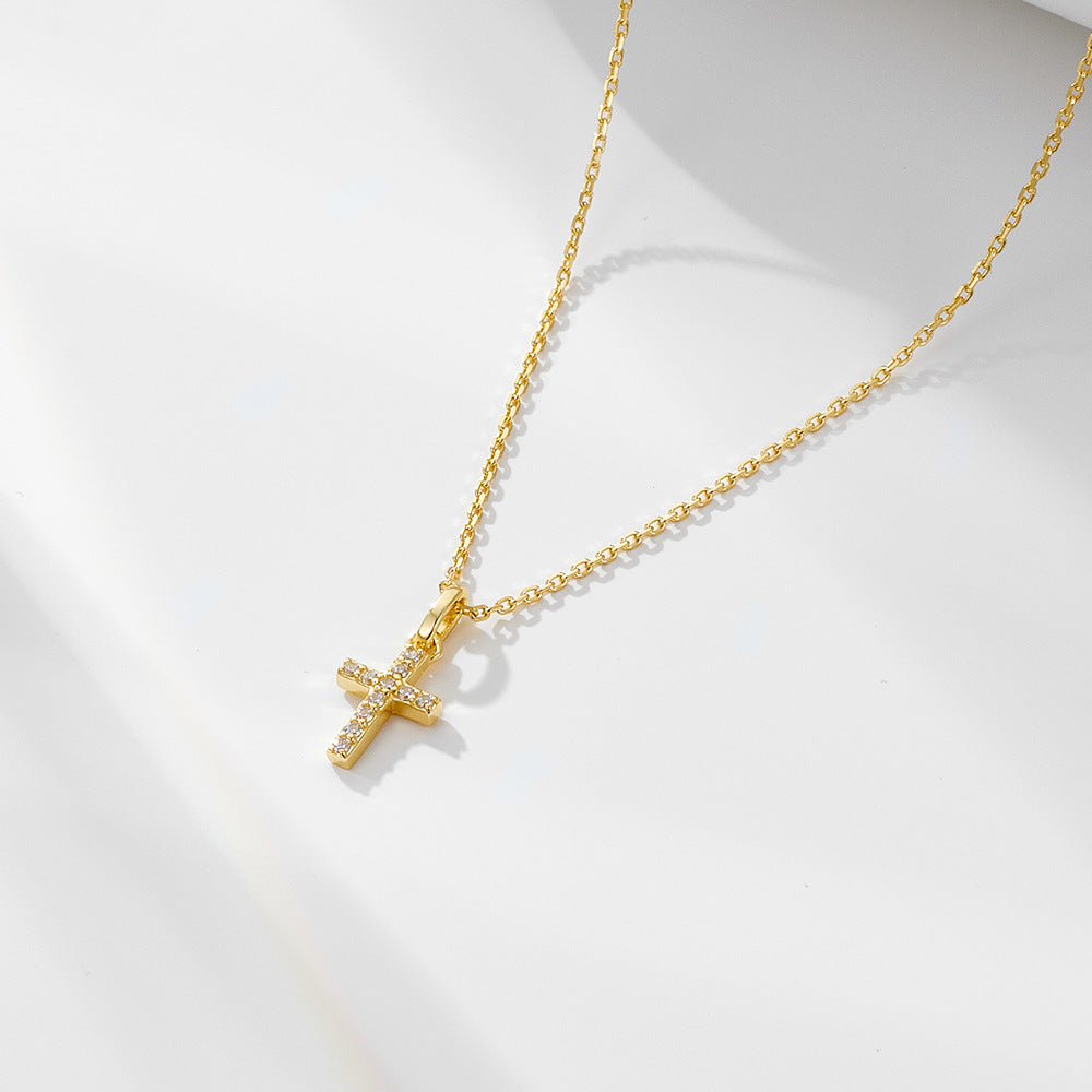 Gold cross pendant necklace with diamond pavé setting on delicate chain, displayed on white surface with subtle shadow casting