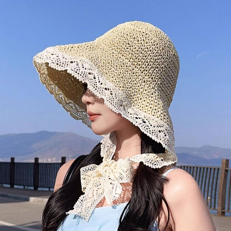 Woman wearing a beige crocheted sun hat with lace trim and a tie, standing outdoors against a blue sky.