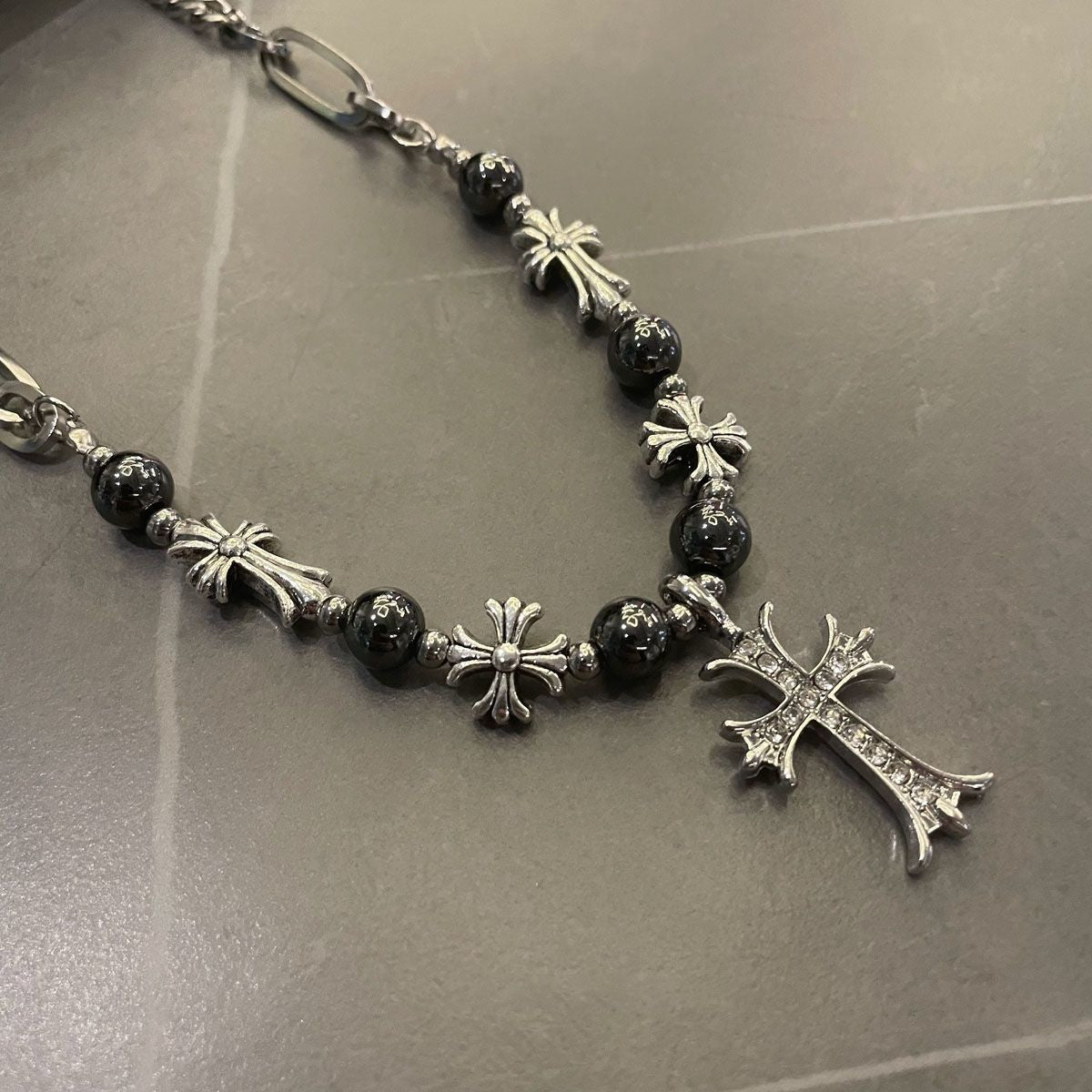 Close-up of silver necklace featuring black beads and decorative crosses on dark surface