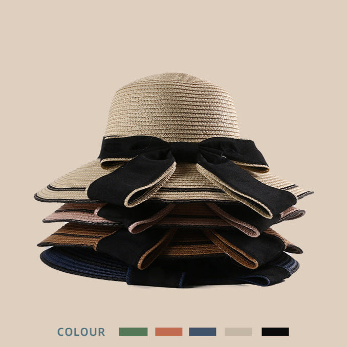 A stacked display of multiple woven straw sun hats in different colors, each featuring a large black bow.