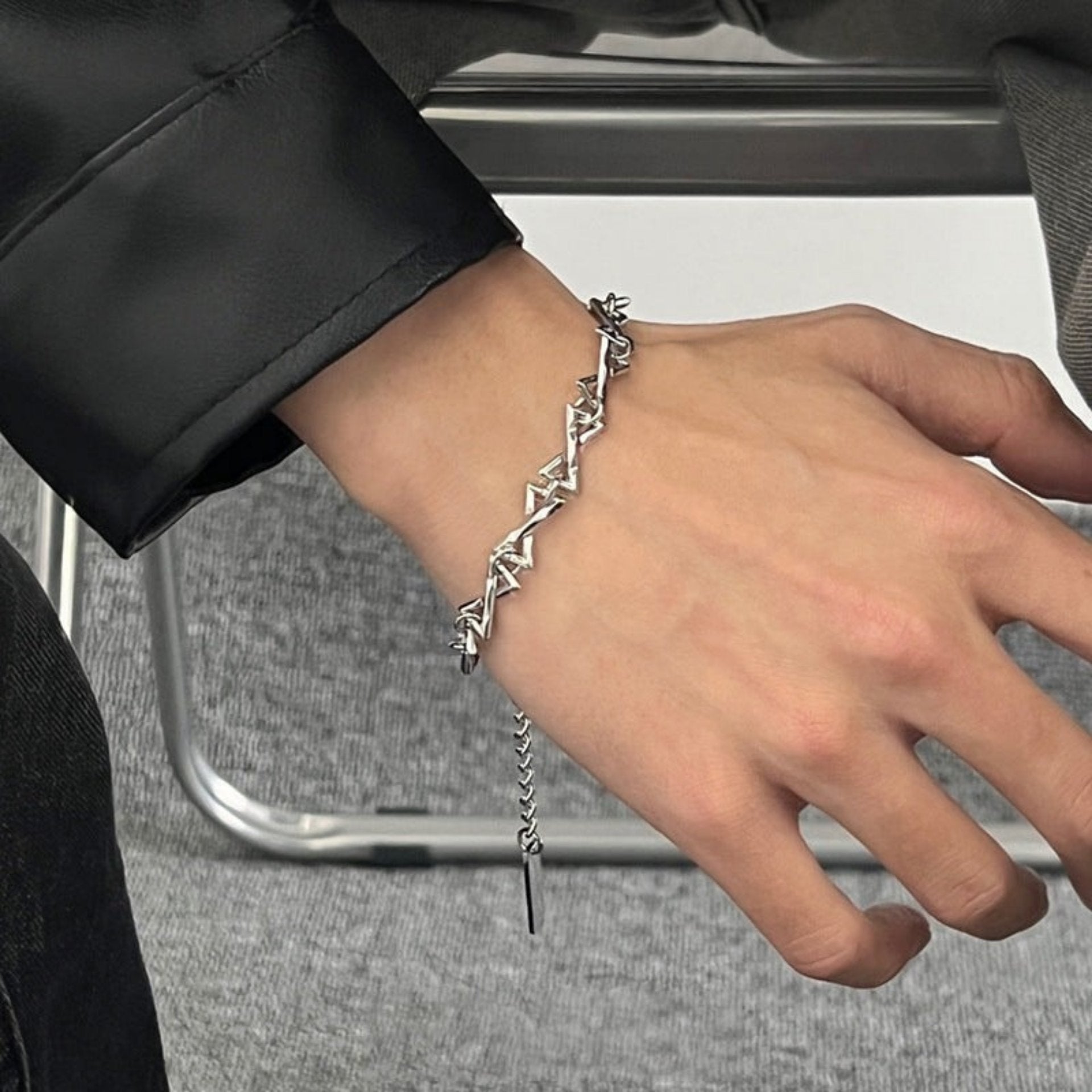 Men’s geometric stainless steel bracelet with sharp angular links, worn on wrist with a black leather jacket for a sleek look.