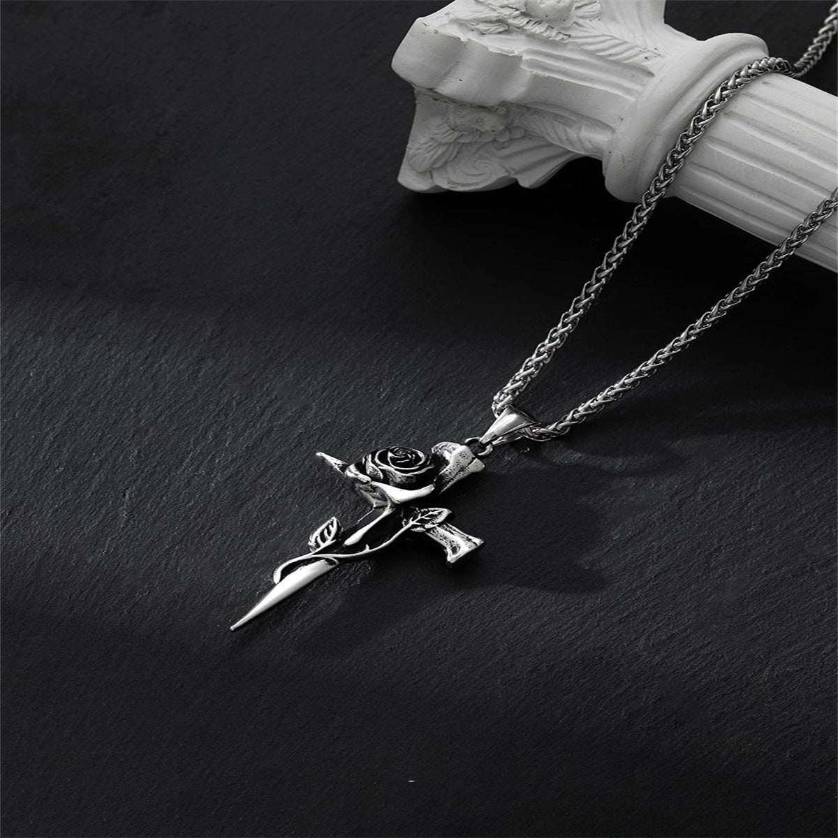 Silver rose cross pendant necklace with detailed flower accent on box chain displayed against black slate with white column