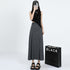 Model wearing asymmetric black crop top and gray maxi skirt with pleated detail, styled with platform sandals and baseball cap