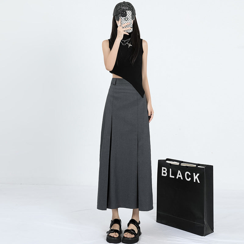 Model wearing asymmetric black crop top and gray maxi skirt with pleated detail, styled with platform sandals and baseball cap