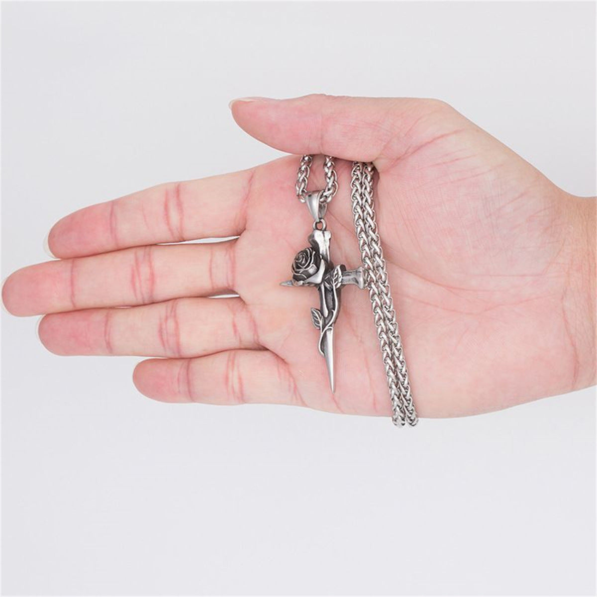 A hand holding silver rose cross pendant necklace with vine detail and sturdy box chain against white background