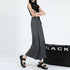Side view highlighting pleated detail and flow of gray maxi skirt, shown with asymmetric black top and platform sandals