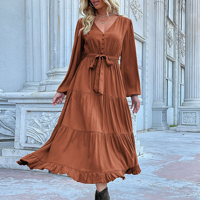 A model is posing in a terracotta button-front maxi dress with tiered skirt, balloon sleeves, tie waist and ruffle hem against classical architecture