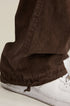 Close-up of brown pants hem with drawstring closure detail at ankle and white sneaker
