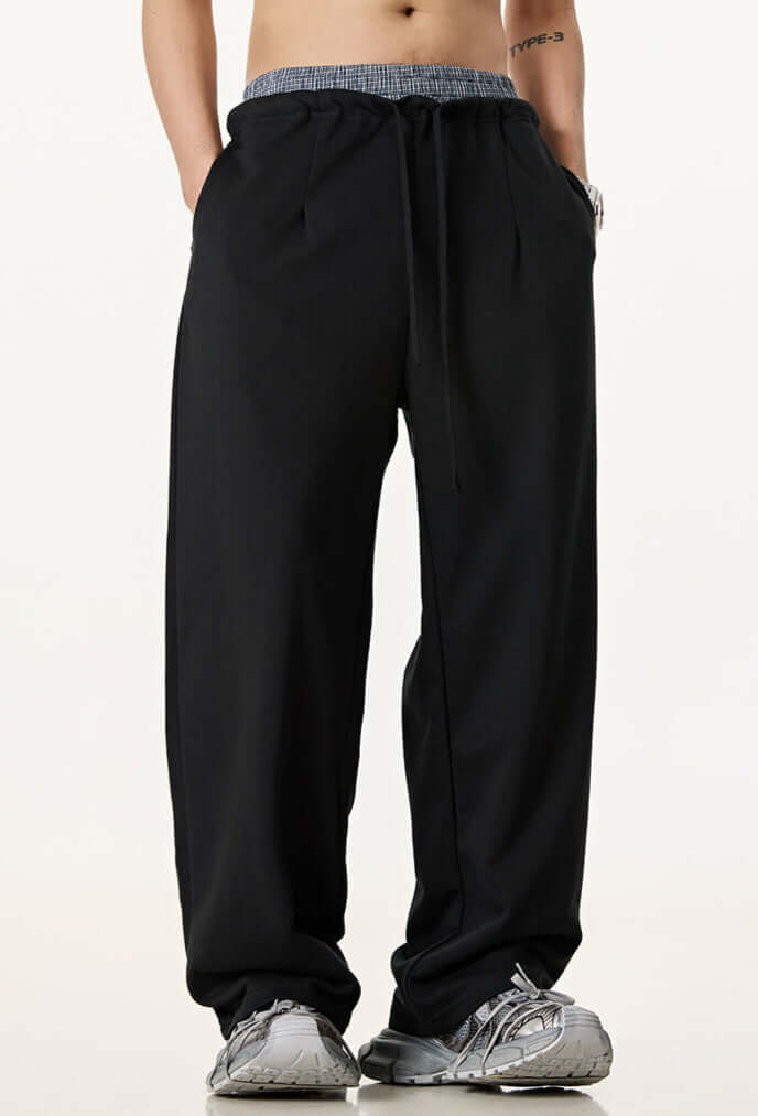 Male model in black wide-leg sweatpants with a contrast waistband, styled with grey sneakers for a casual streetwear look.