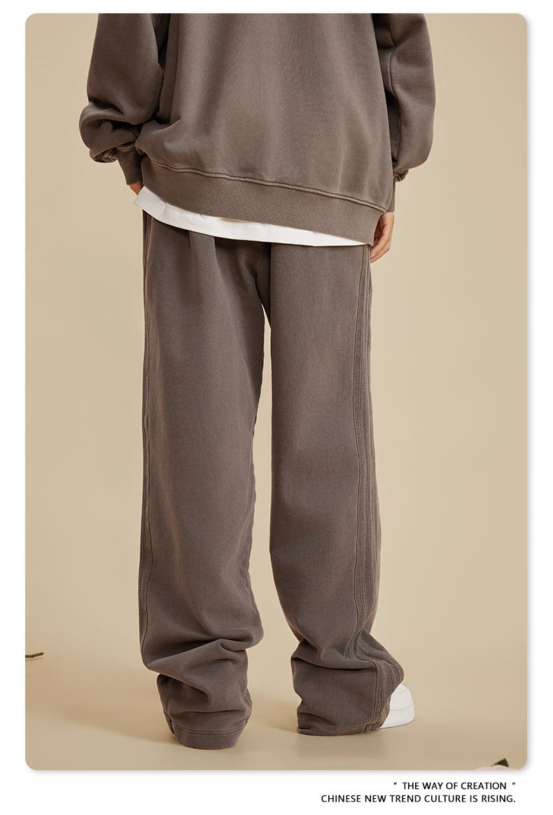 Back view of person wearing grey sweatshirt with white underlayer and wide-leg sweatpants on beige background