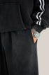 Close-up of black hoodie sleeve with silver watch and hand in pocket of black sweatpants