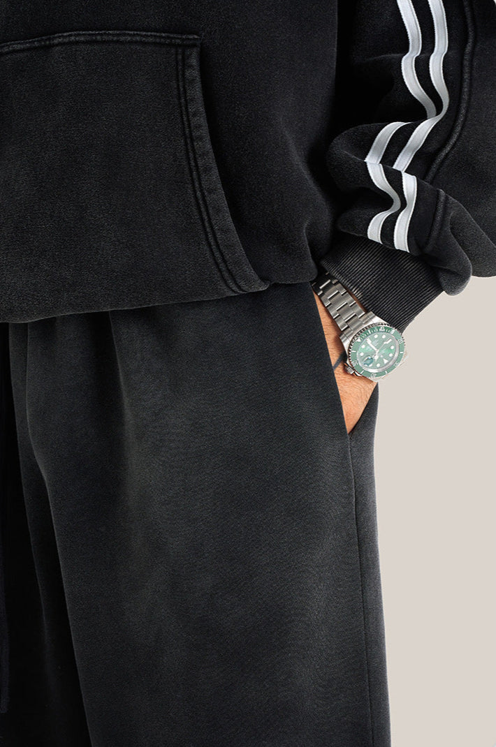 Close-up of black hoodie sleeve with silver watch and hand in pocket of black sweatpants