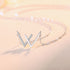 Side view of silver W necklace with sparkling crystal detail against soft pink backdrop