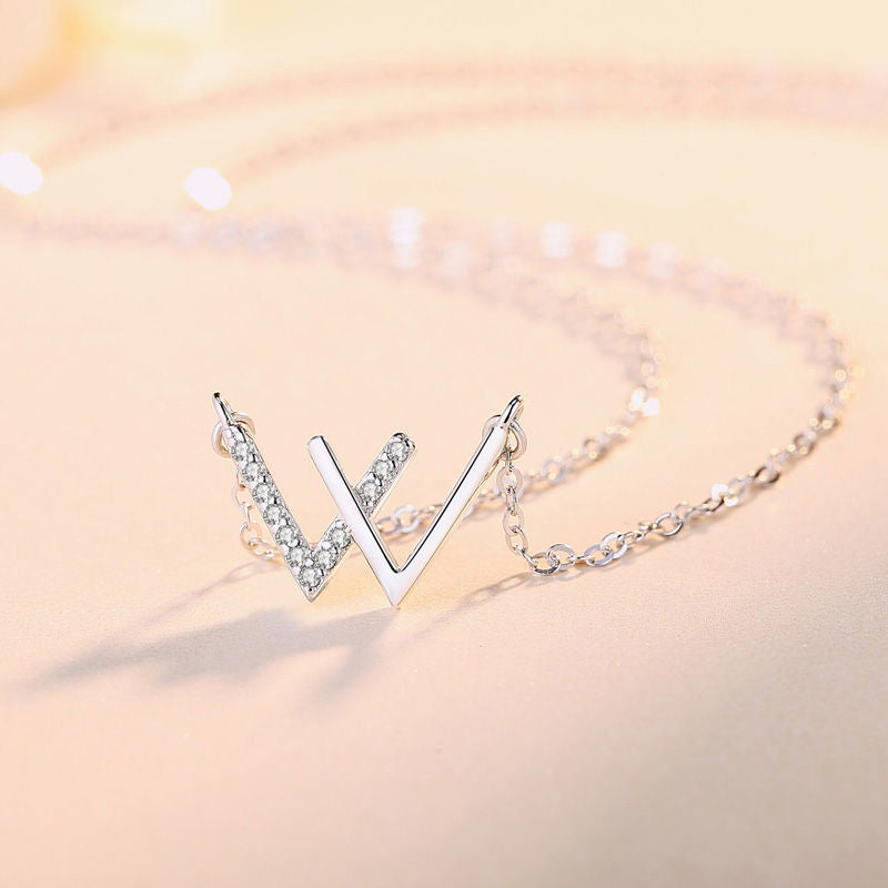 Side view of silver W necklace with sparkling crystal detail against soft pink backdrop