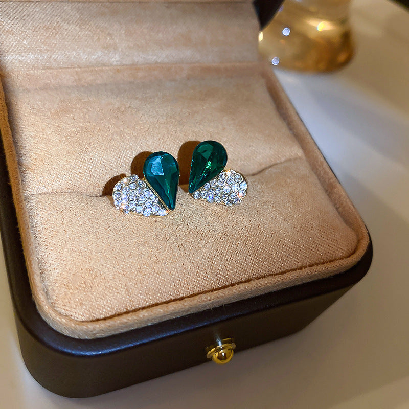 Heart-shaped earrings with green gemstone and crystal elements displayed in jewelry box showing elegant mixed-material design