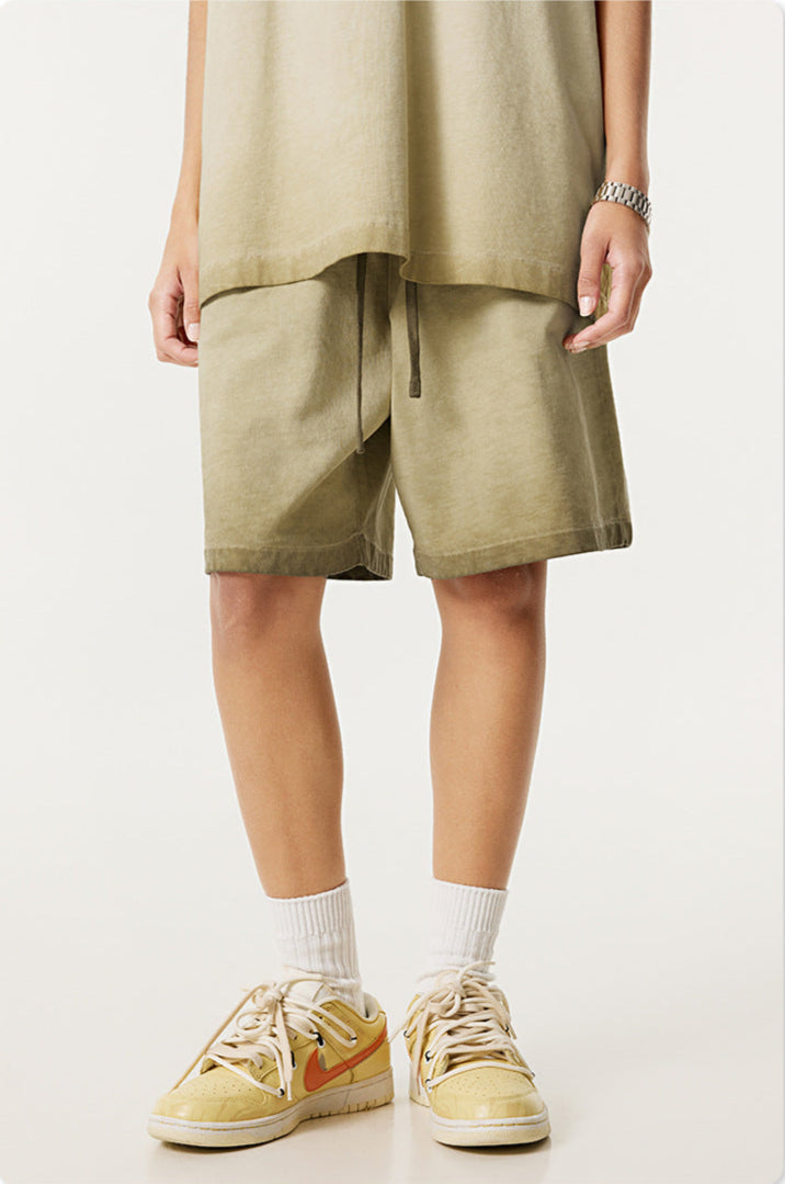 A person wearing light sage green shorts with matching top, silver watch and cream athletic shoes against white background